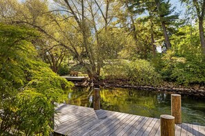 Eine Holzterrasse mit einer Bank, umgeben von üppigem Grün und einer ruhigen Wasseroberfläche.