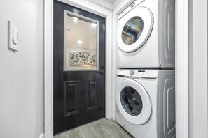 A laundry room with a black door, two stacked washing machines, and a tiled floor. - Beautiful Buckhead Unit + Direct MARTA to World Cup Stadium + King Bed (Atlanta)