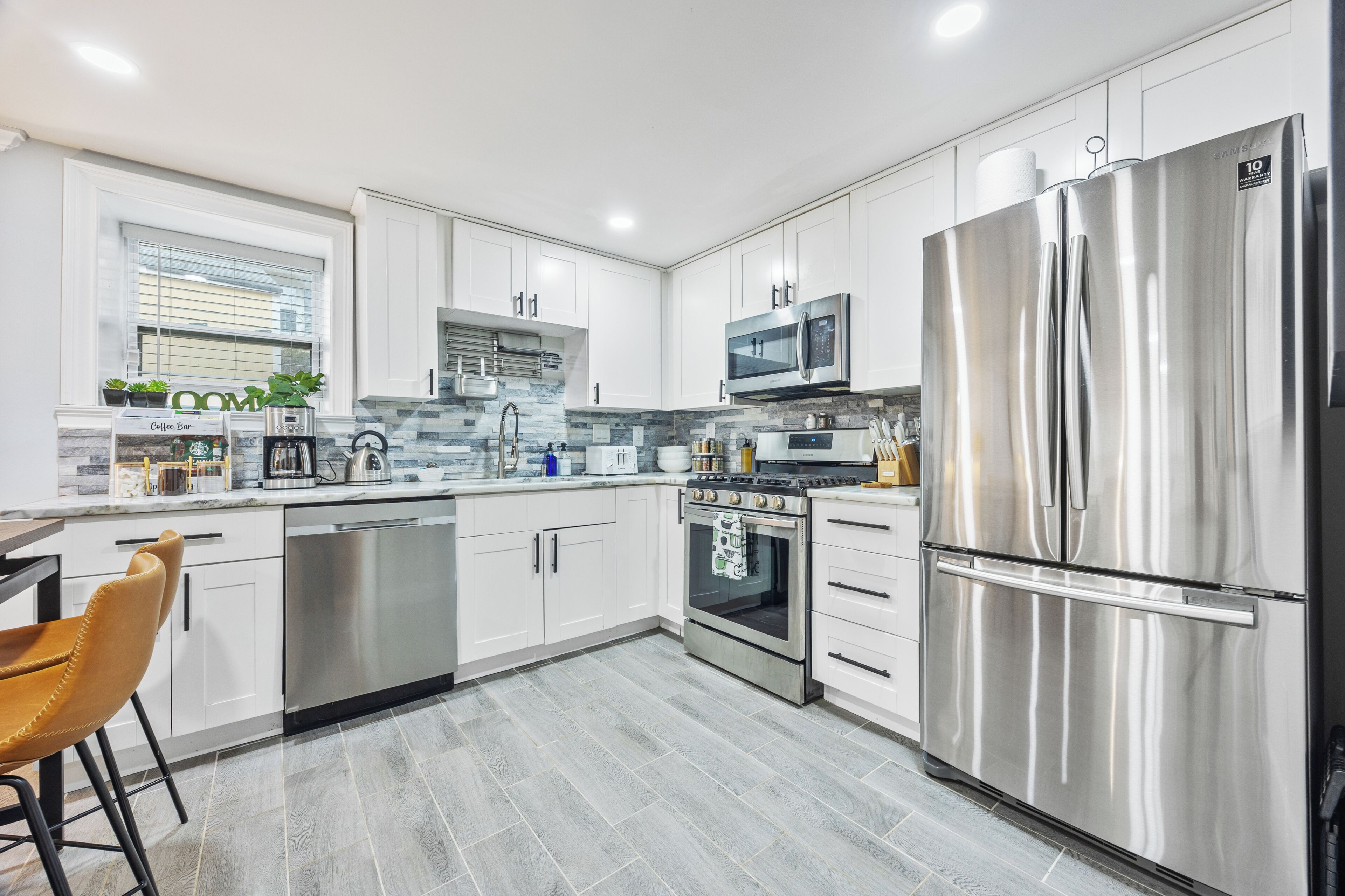 A modern kitchen with stainless steel appliances, white cabinetry, and a grey tiled floor.