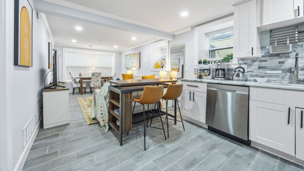 Een moderne keuken met witte kasten, een roestvrijstalen vaatwasser en een eethoek met een tafel en stoelen.