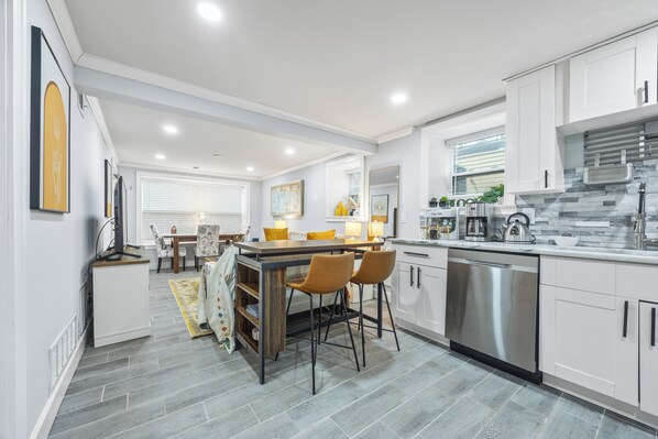 A modern kitchen with white cabinetry, a stainless steel dishwasher, and a dining area with a table and chairs. - Beautiful Buckhead Unit + Direct MARTA to World Cup Stadium + King Bed (Atlanta)
