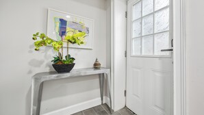 Een hal met een witte deur, een lijst met een abstract schilderij, een potplant en een klein decoratief object op een console tafel.