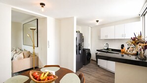 Eine moderne Küche mit weißen Schränken, einem schwarzen Kühlschrank und einem Essbereich mit Holztisch und Stühlen.