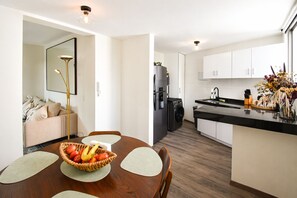 A modern kitchen with white cabinets, a black refrigerator, and a dining area with a wooden table and chairs. - It's Always Sunny in this Roma Norte Apartment (Mexico City)