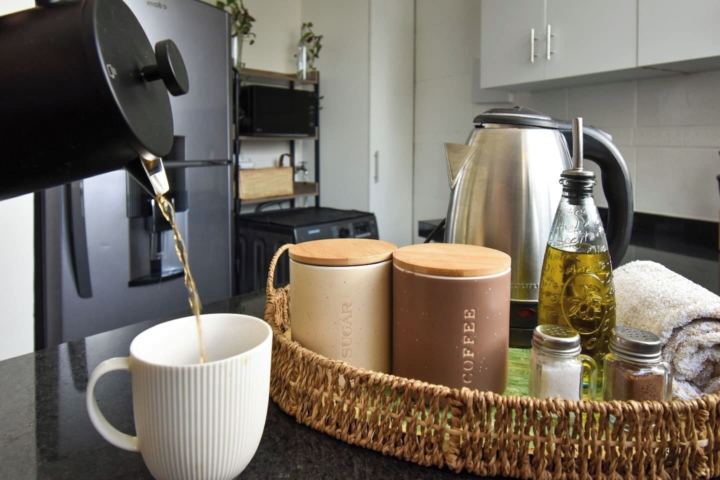 A kitchen with a coffee maker, a kettle, a bottle of oil, and two containers labeled 'COFFEE' and 'SUGAR' on a counter.