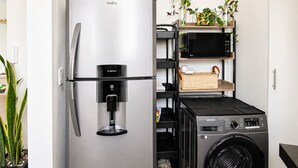 Eine kompakte Küche mit einem Edelstahlkühlschrank, einer eingebauten Mikrowelle und einer Samsung Waschmaschine.