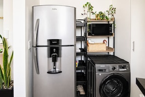 A compact kitchen with a stainless steel refrigerator, a built-in microwave, and a Samsung washing machine. - It's Always Sunny in this Roma Norte Apartment (Mexico City)