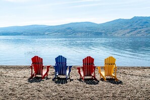 Quatre chaises Adirondack sur une plage de galets, avec un lac et des montagnes en arrière-plan.