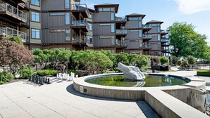 A modern multi-story building with balconies, a central courtyard with a fountain, and surrounding greenery.