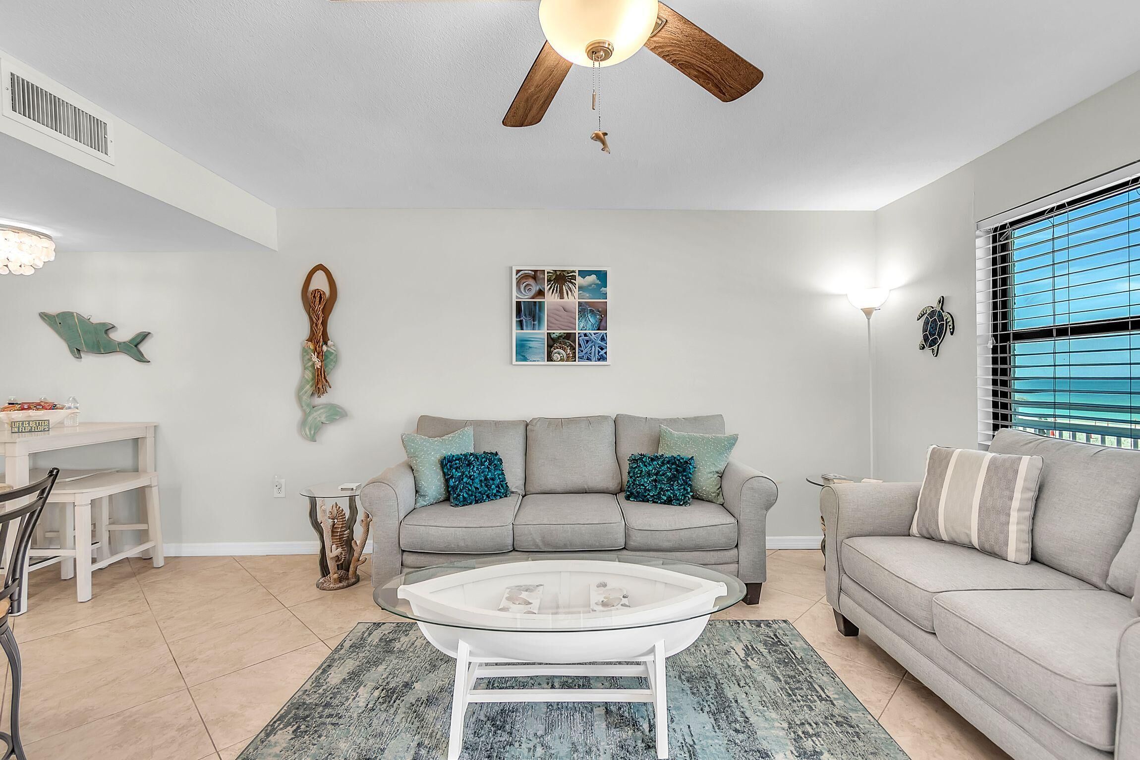 A living room with a ceiling fan, a gray sofa, a white coffee table, and a dining area with a white table and chairs.