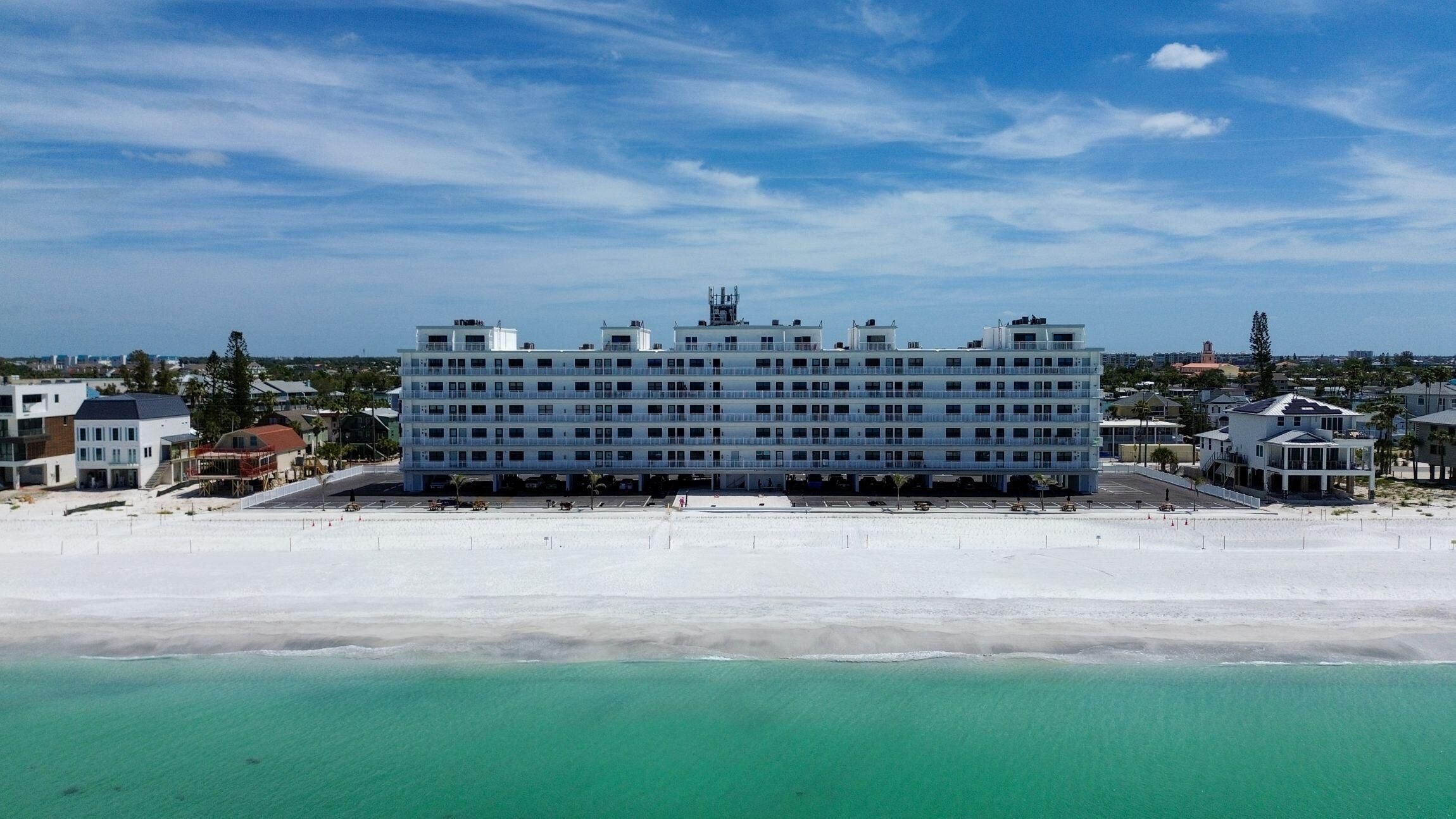Um hotel com vários andares e telhado plano, situado ao lado de uma praia com águas azul-turquesa cristalinas.