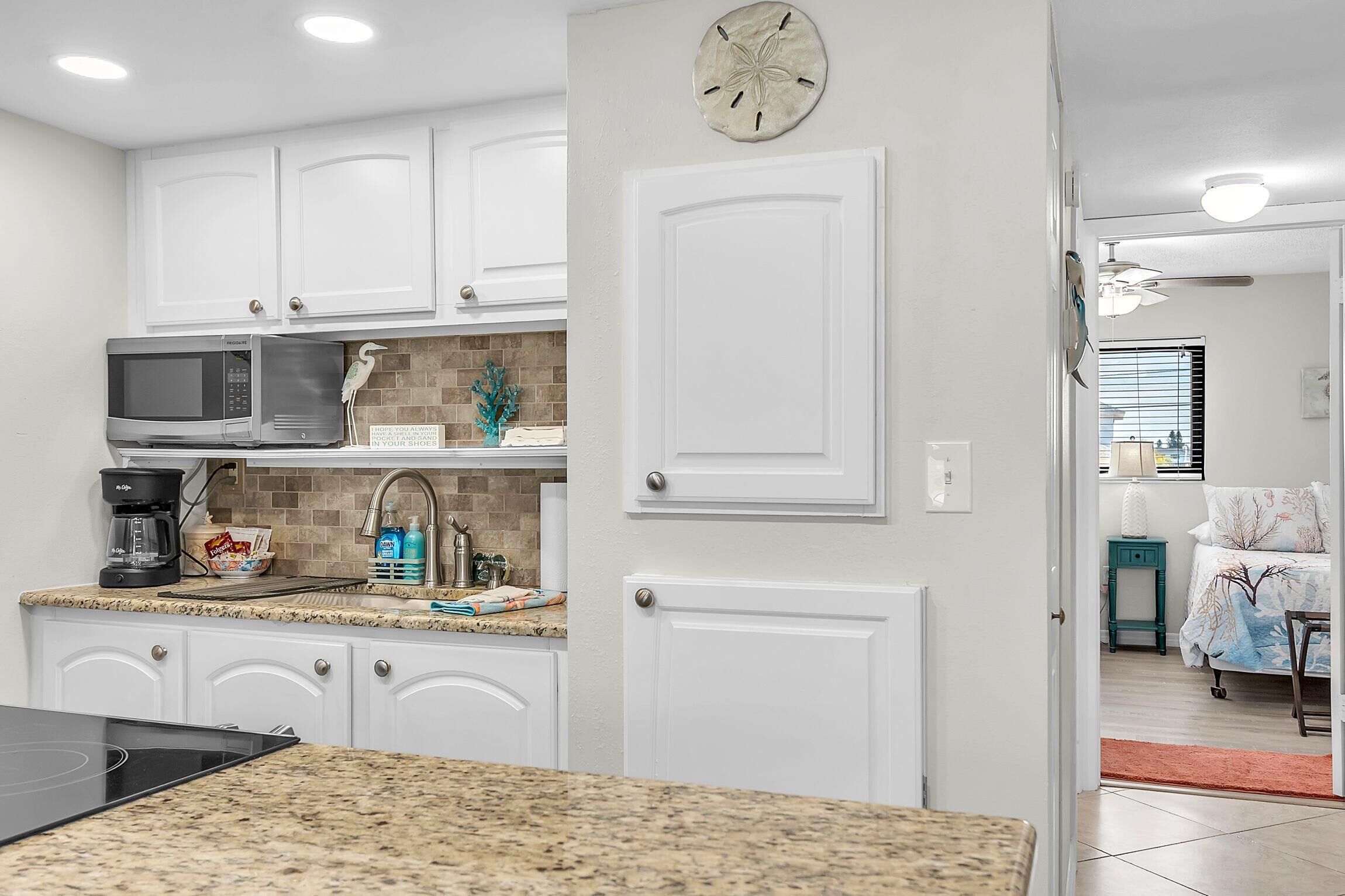 A kitchen with white cabinets, a microwave, a coffee maker, and a sink.