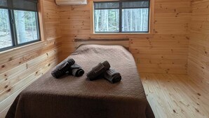 Una habitación de cabaña de madera con una cama, dos ventanas, un ventilador de techo y un equipo de aire acondicionado.