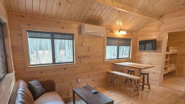 Interior de una cabaña con techo de madera, un sofá, una mesa y un ventilador de techo.