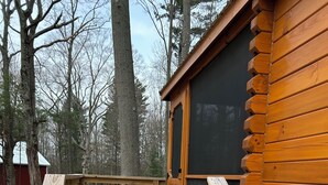 Una escalera de madera lleva a una cabaña con puerta negra, rodeada de árboles.