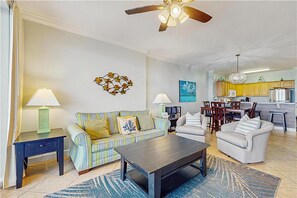 A living room with a sofa, armchairs, a coffee table, and a dining area with chairs and a table. - Tropic Winds 1003 (Panama City Beach)