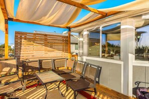 An outdoor seating area with tables and chairs, a wooden slatted partition, and large windows. - Oceanfront | Game Room | Clamming | Deck (Ocean Shores)