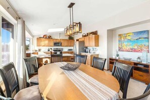 A modern kitchen with wooden cabinets, a dining table with chairs, and a pendant light. - Oceanfront | Game Room | Clamming | Deck (Ocean Shores)