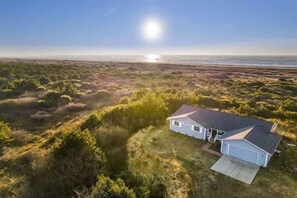 A single-story house with a garage, surrounded by dense vegetation and a clear view of the ocean. - Oceanfront | Game Room | Clamming | Deck (Ocean Shores)