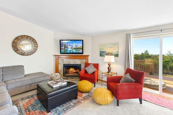 A living room with a fireplace, a television, and a large window with a view. - Oceanfront | Game Room | Clamming | Deck (Ocean Shores)