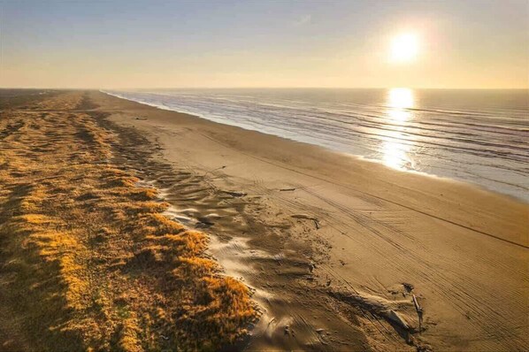 A beach with a clear sky and the sun low on the horizon.