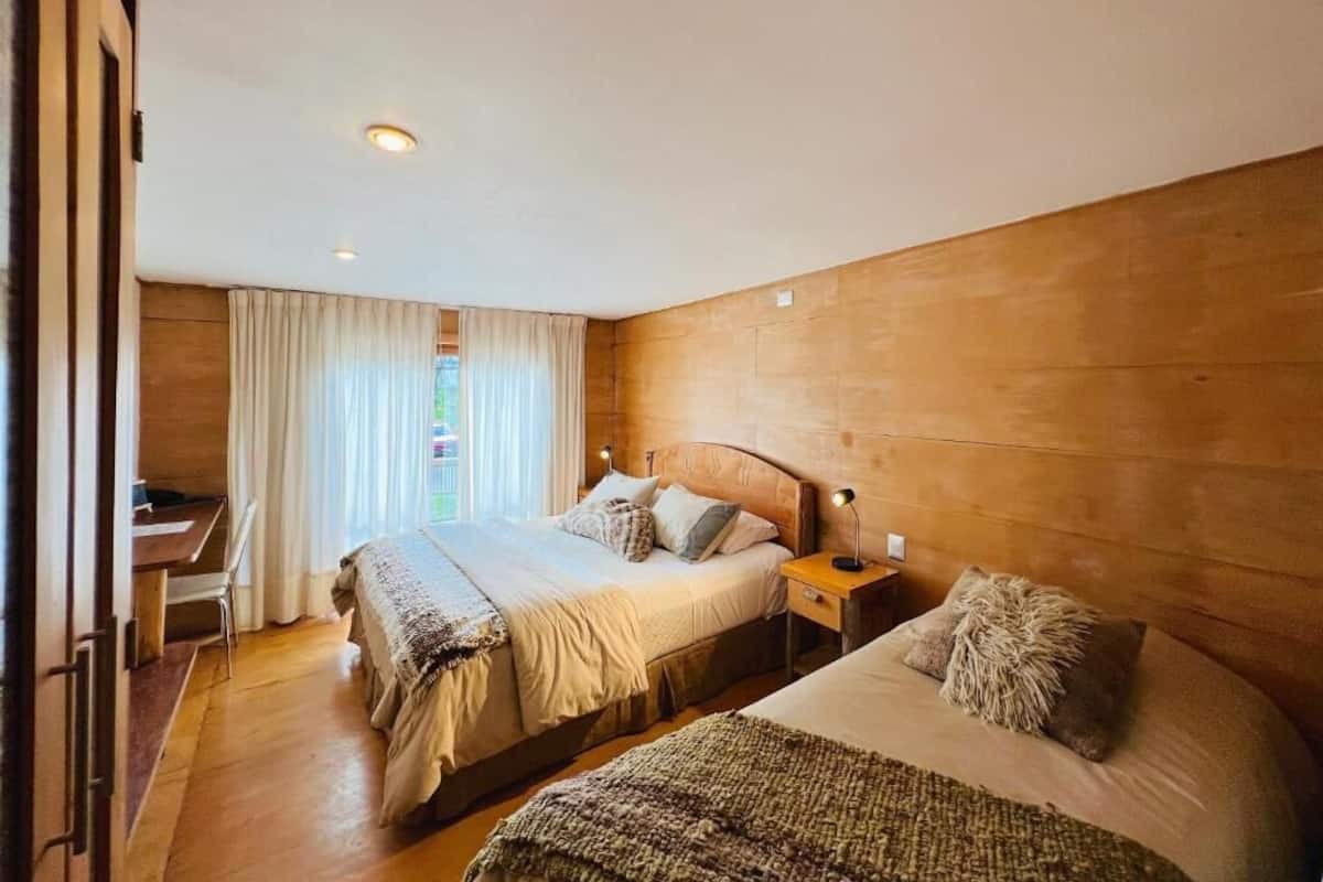 A bedroom with two beds, a desk, and a window with curtains.