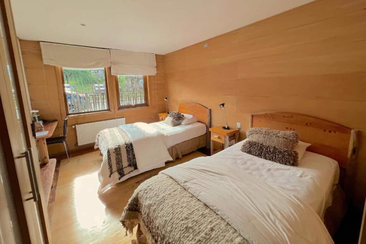 A bedroom with two beds, wooden walls, a window, and a radiator.