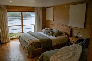 Un dormitorio con un ventanal grande, una cama, una mesita de noche y un cabecero de madera.
