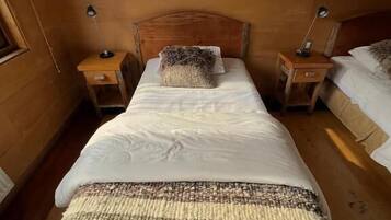 Habitación con cama de cabecera de madera, dos mesitas de noche con lámparas, una manta tejida y suelo de madera.