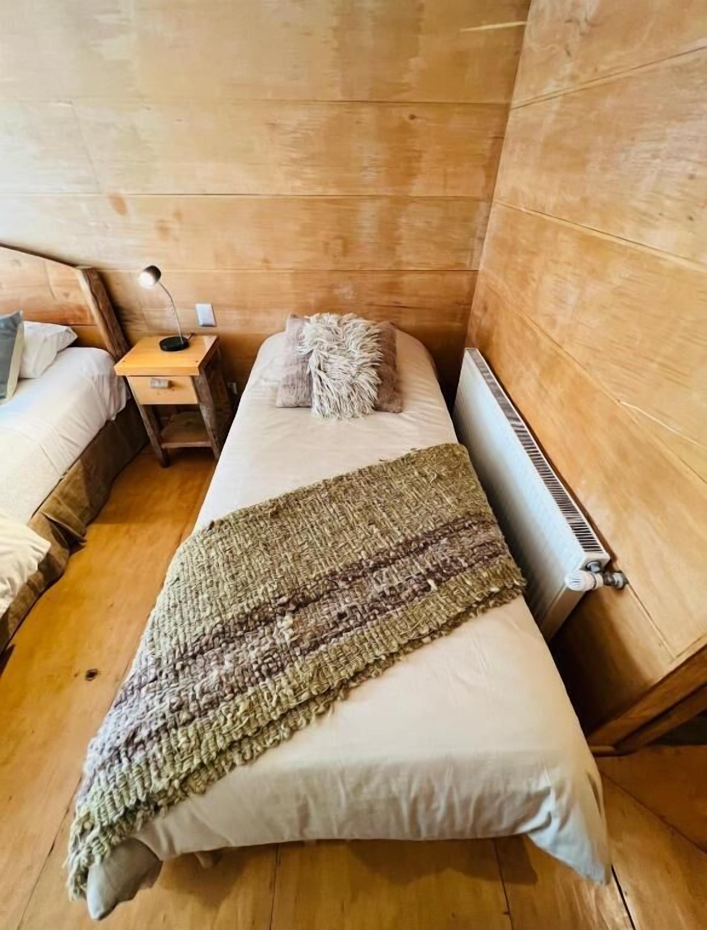 Una habitación acogedora de estilo cabaña con una cama individual, una mesita de noche, una lámpara y un radiador.