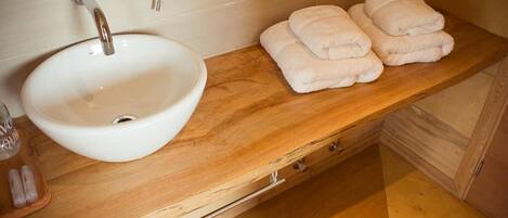 Un baño con lavamanos blanco, tocador de madera y toallas ordenadas.
