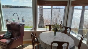 A room with a view of a lake, a dining table with chairs, a leather armchair, and a window with blinds. - Lakefront Home near Alpena Includes Kayaks, Canoe, Rowboat.  Sleeps up to 6 (Alpena)