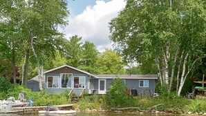 A lakeside cabin with a dock, surrounded by trees. - Lakefront Home near Alpena Includes Kayaks, Canoe, Rowboat.  Sleeps up to 6 (Alpena)