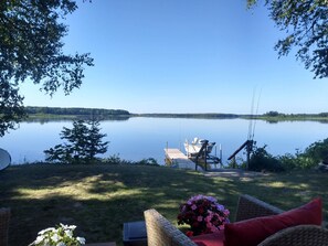 A lakeside view with a dock, a boat, and a wicker chair with a flower arrangement. - Lakefront Home near Alpena Includes Kayaks, Canoe, Rowboat.  Sleeps up to 6 (Alpena)