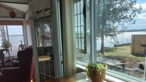 A room with a wooden table, a potted plant, and a view of a lake. - Lakefront Home near Alpena Includes Kayaks, Canoe, Rowboat.  Sleeps up to 6 (Alpena)