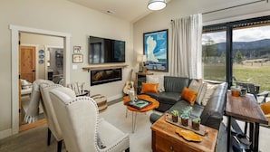 A living room with a sofa, chairs, a coffee table, a TV, a fireplace, and a view of the outdoors. - New! Retreat with Hot Tub and Mountain Views near Bozeman! (Gallatin Gateway)