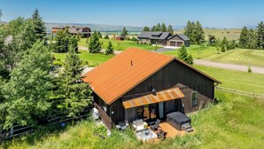 A large wooden cabin with a sloped roof, surrounded by a well-maintained lawn and trees. - New! Retreat with Hot Tub and Mountain Views near Bozeman! (Gallatin Gateway)