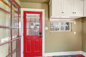 Une porte rouge avec un panneau de verre, un meuble blanc au-dessus, et une fenêtre donnant sur des maisons.