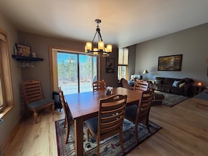 Amplia sala de estar con mesa de comedor, sillas, sofá y un ventanal con vistas a árboles.