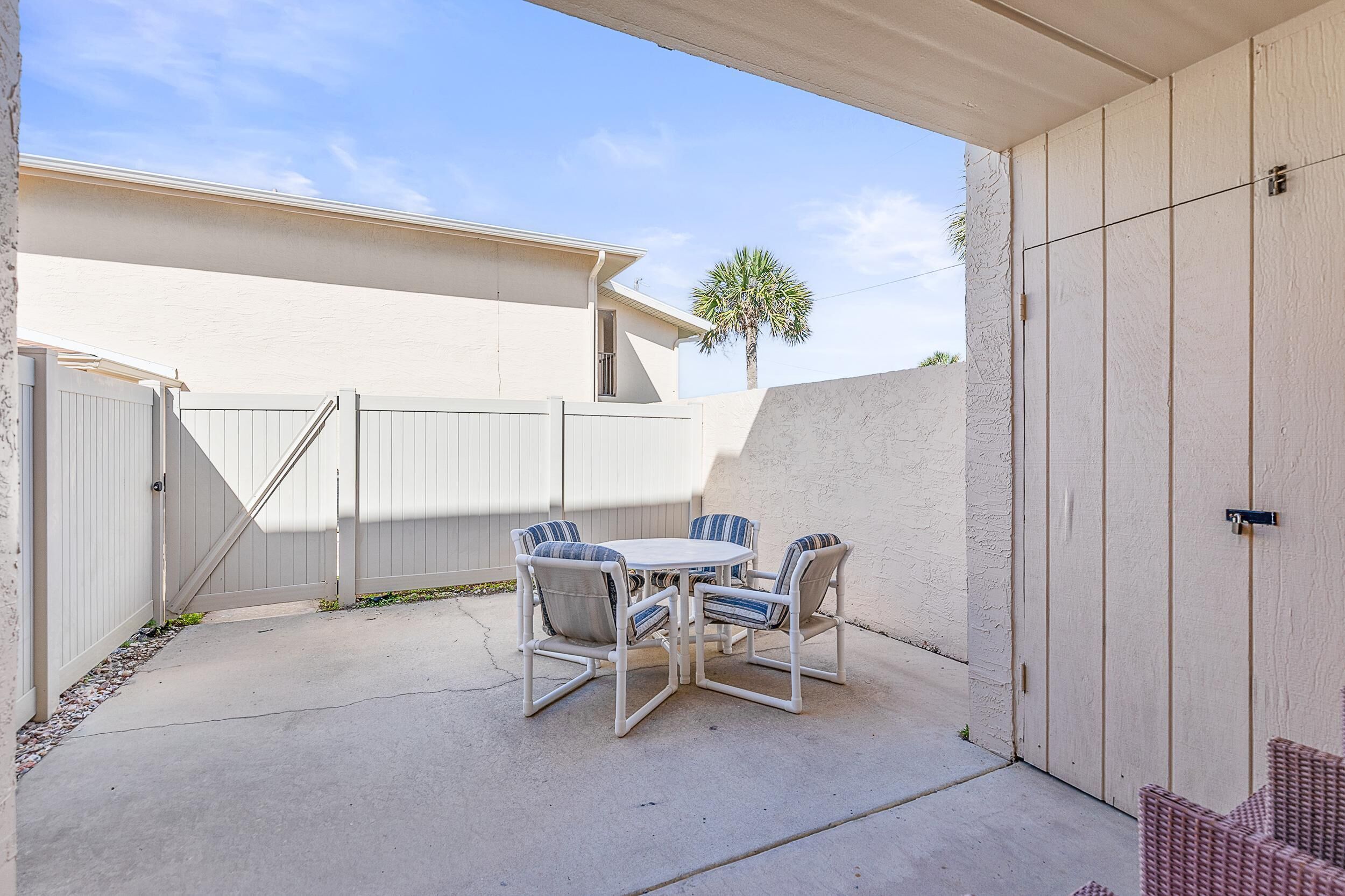 A patio with a table and chairs, a white fence, and a palm tree.