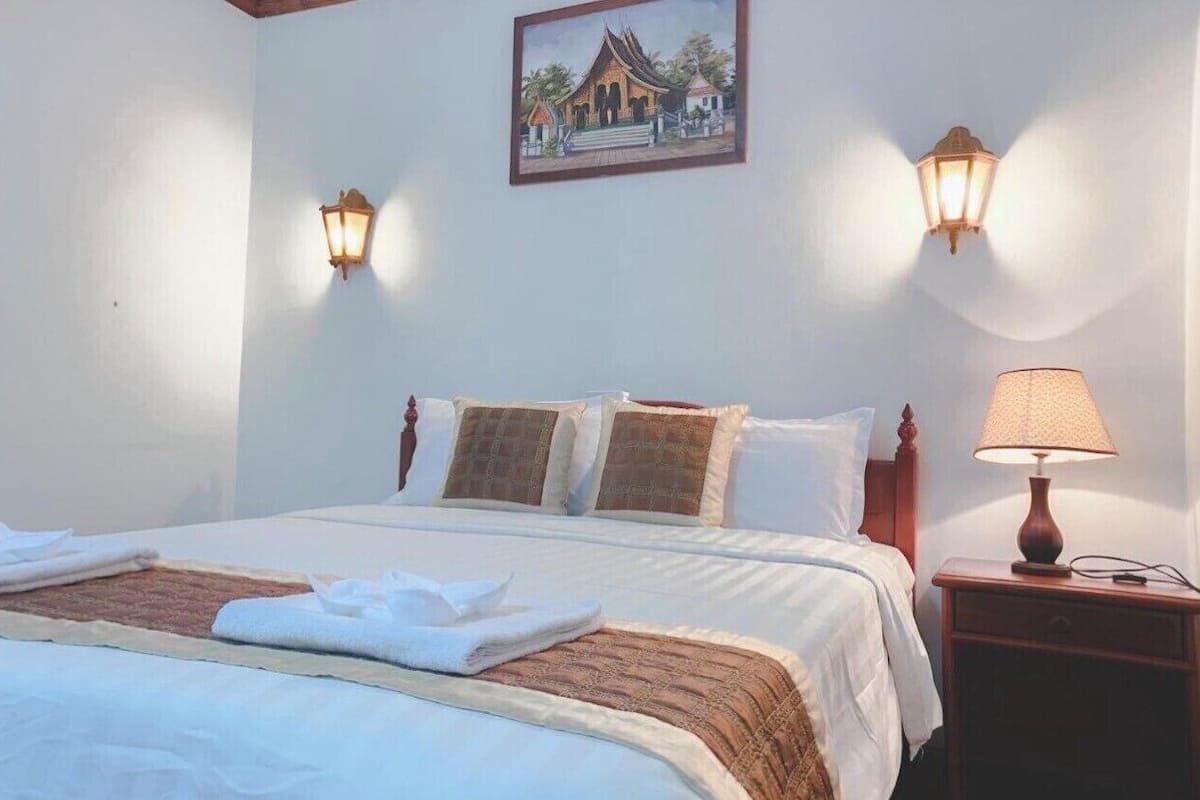 Una cama bien tendida con almohadas, una mesita de noche con lámpara y un cuadro colgado en la pared.