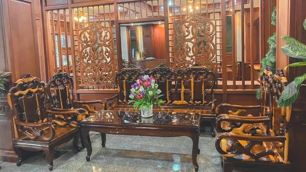 A traditional wooden room with ornate furniture, a central table with a vase of flowers, and a decorative screen. - Khampiane Hotel (Vientiane)