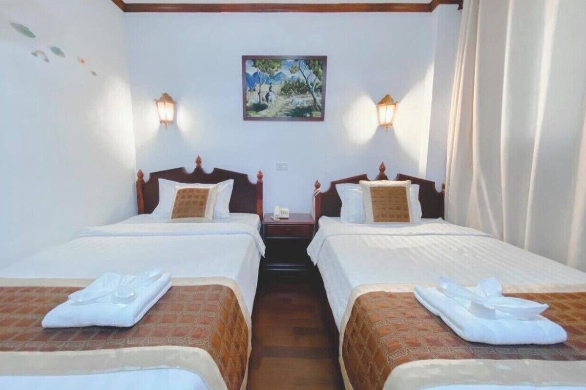 Una habitación de hotel con dos camas, un cuadro en la pared y dos lámparas de pared.