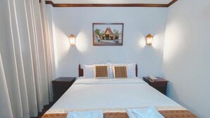 A hotel room with a bed, two bedside tables, a nightstand, a wall-mounted picture, and a curtain. - Khampiane Hotel (Vientiane)