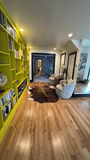 Ein Wohnzimmer mit Holzboden, einem gelben Bücherregal, einem Cowhide-Teppich und einer blauen Wand mit Muster.