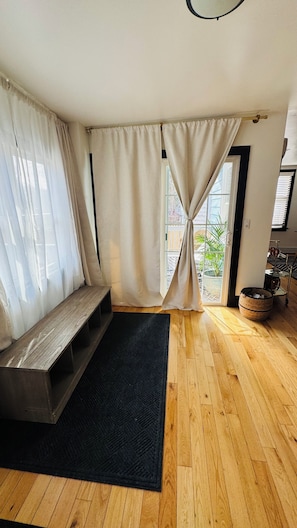 A room with a wooden bench, a black rug, and a large window with curtains.