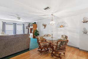 A living room with a sofa, dining table, wicker chairs, ceiling fans, and wall decorations. - Oasis 18 (Daytona Beach)