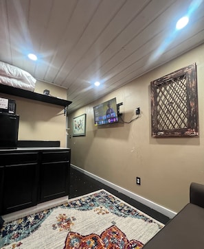 A room with a bed, a TV mounted on the wall, a desk with a computer, and a patterned rug on the floor. - Cozy 1-bedroom studio in lovely Dallas with AC (Dallas)