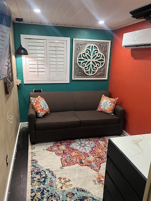 A room with a brown sofa, decorative wall art, a patterned rug, and a white air conditioning unit. - Cozy 1-bedroom studio in lovely Dallas with AC (Dallas)