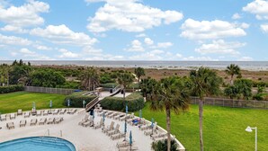 A pool area with lounge chairs and umbrellas, a view of the beach, and a clear sky. - Updated Direct Oceanfront Condominium with Great Amenities (St. Simons Island)